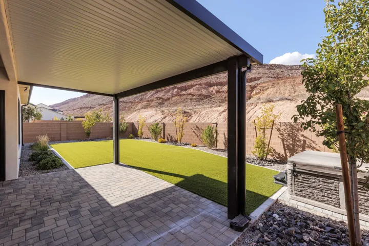 Covered patio with paver flooring, artificial turf, and a stone-clad built-in structure