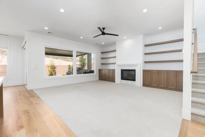 Spacious living area featuring a fireplace, built-in cabinetry, recessed lighting, a ceiling fan, and large windows