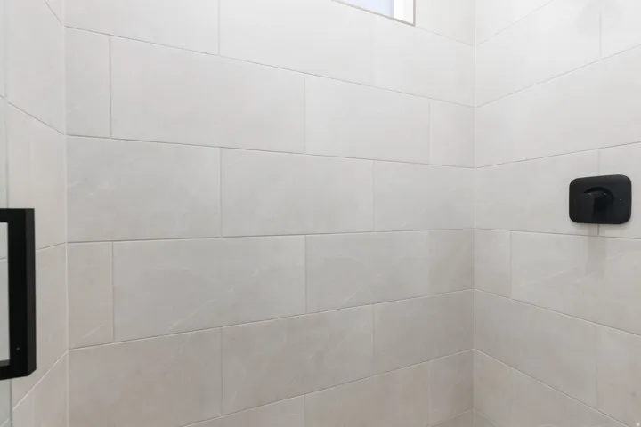 Shower enclosure featuring large format light-toned tile, matte black shower control, and a glass partition with a black frame