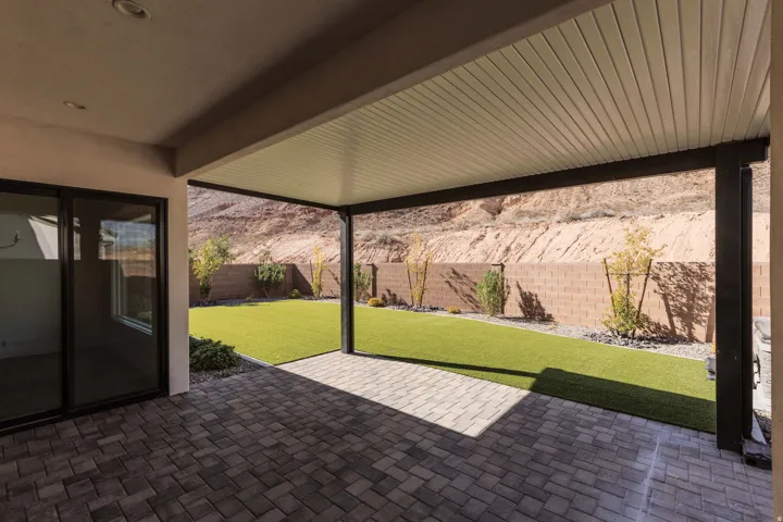 Covered patio with paver flooring, leading to artificial turf landscaping, and a block wall perimeter