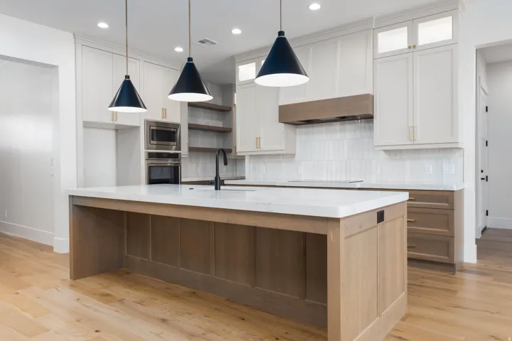 Gourmet kitchen featuring a central island with a white countertop, light wood-finish cabinetry, stainless steel built-in appliances, and pendant lighting