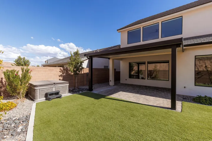 Expansive backyard featuring artificial turf, a built-in hot tub, and a covered patio with paver flooring