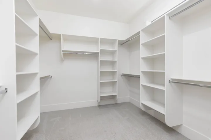 Expansive walk-in closet featuring white built-in shelving, multiple hanging rods, and light-toned carpeting
