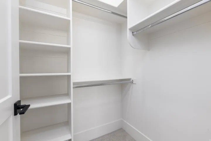 Built-in closet shelving, multiple hanging rods, and light-colored carpeting