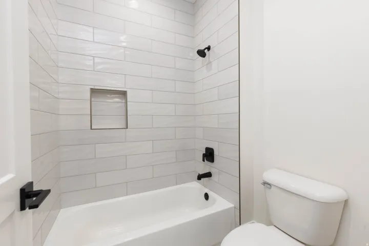 Bathtub with white subway tile surround, matte black fixtures, and a recessed shower niche