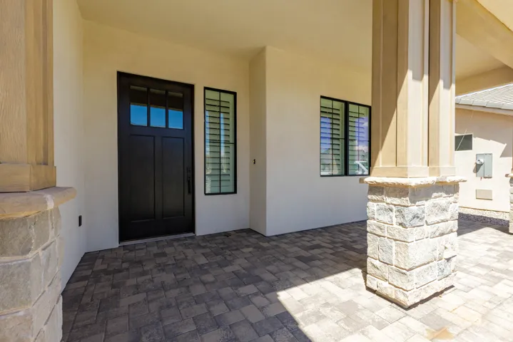 Paved entry with stone-clad columns, a dark panel door with glass inserts, and a side window with louvered shutters