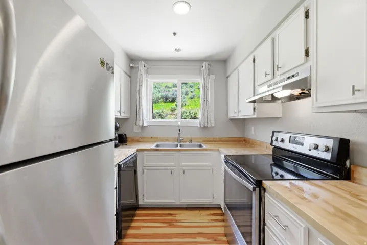 Kitchen featuring bright white cabinetry, wood-finish countertops, stainless steel refrigerator, black electric range, and a dual basin sink
