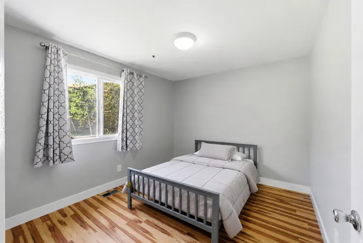 Light-filled room featuring wood-finish flooring, a double window with white trim, a flush-mount ceiling light fixture, and light gray wall paint