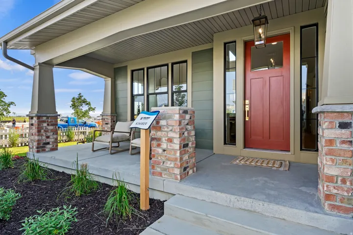 Inviting covered front porch with brick column accents, a red entry door, and dark-framed sidelight windows