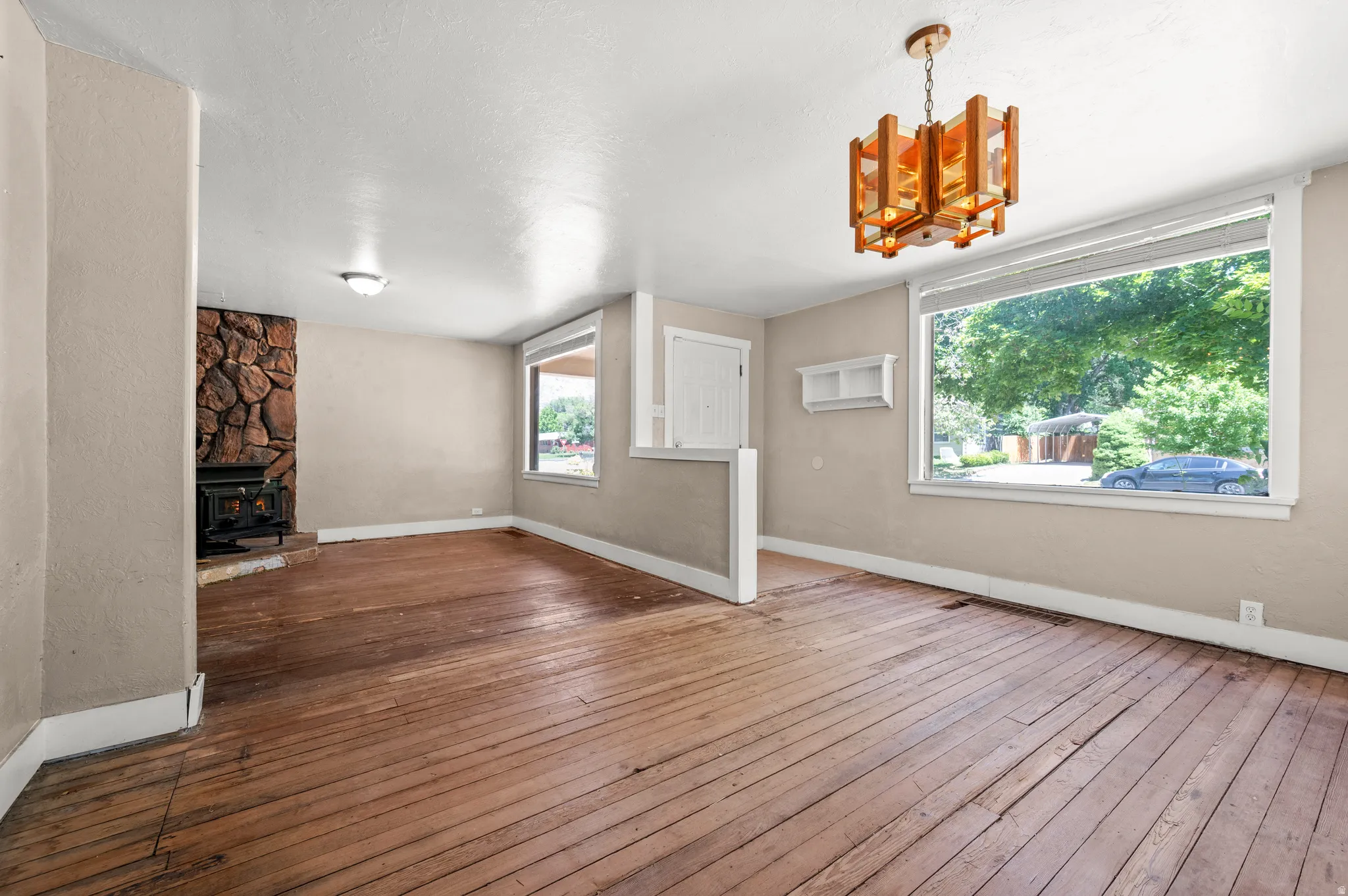 Spacious room featuring exposed wood flooring and a prominent stone-clad fireplace with a wood-burning stove insert