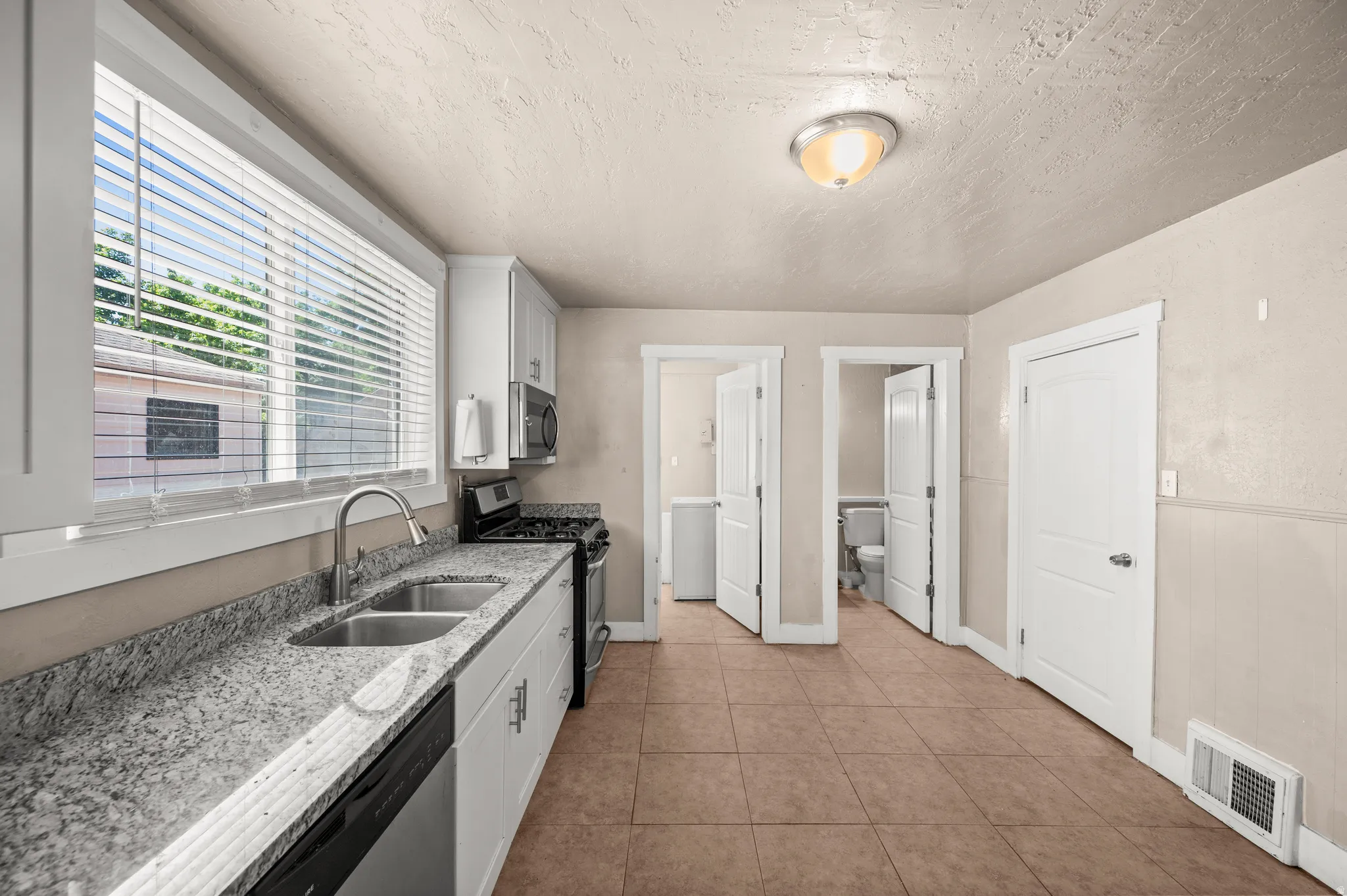 Kitchen featuring a stainless steel dual-basin sink, speckled countertops, white cabinetry, integrated dishwasher, and tile flooring