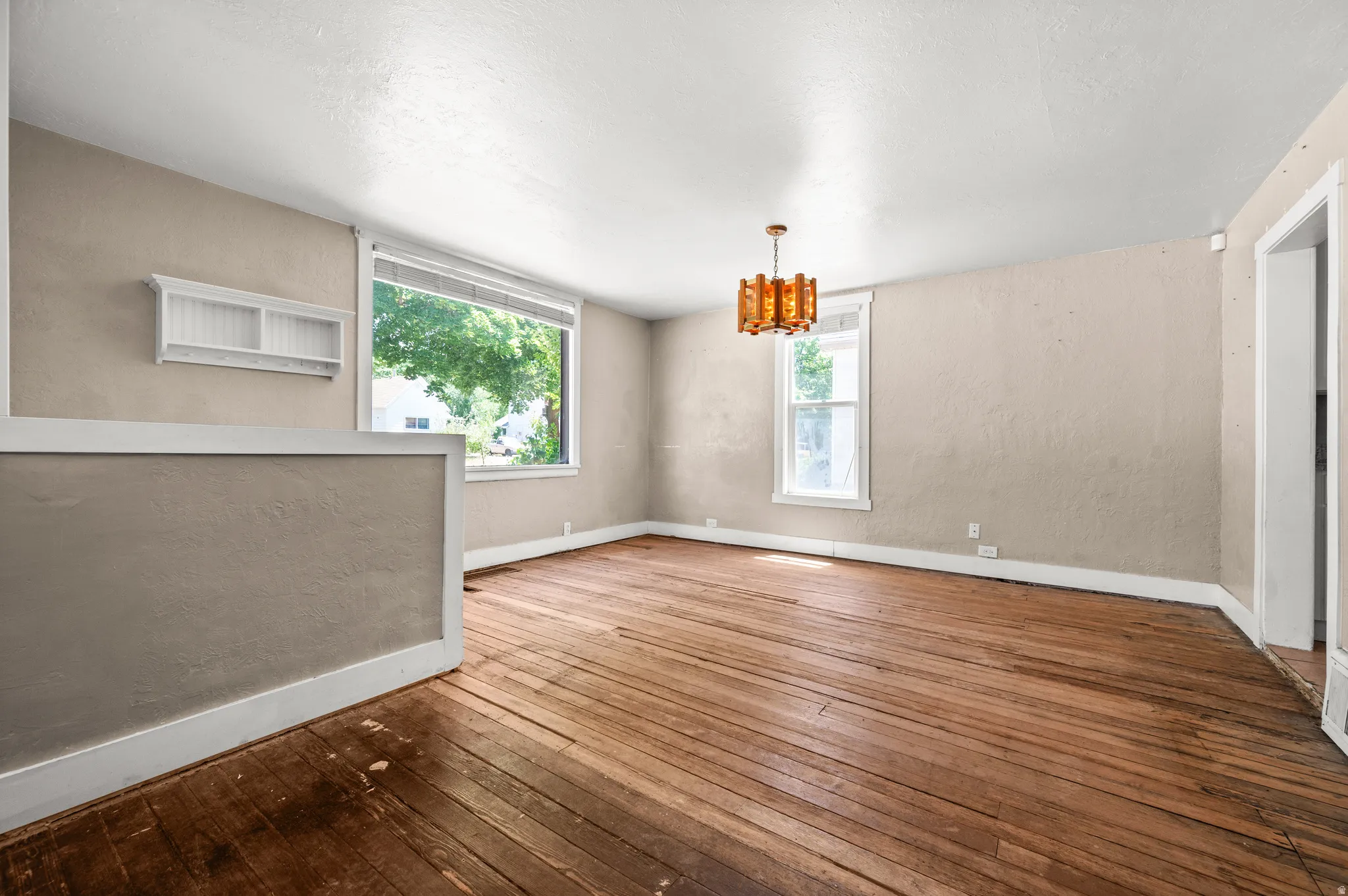 Expansive interior room featuring wide plank wood flooring, a large picture window, a secondary window, and a decorative ceiling light fixture