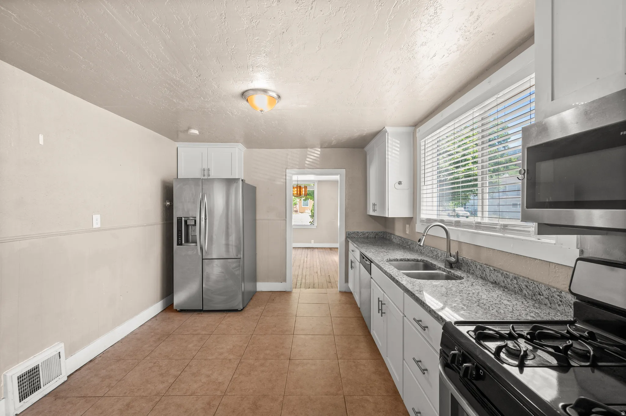 Kitchen featuring tile flooring, white cabinetry, a dual basin sink, a gas range, and a stainless steel microwave