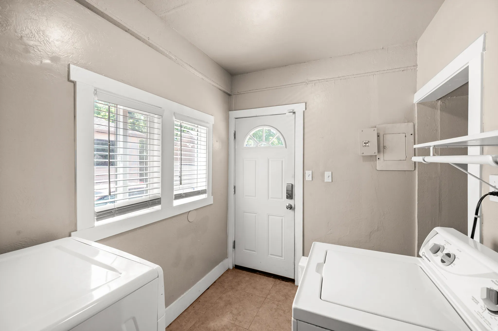 Utility room featuring a window with blinds, a white paneled door with an arched glass insert, and durable tile flooring