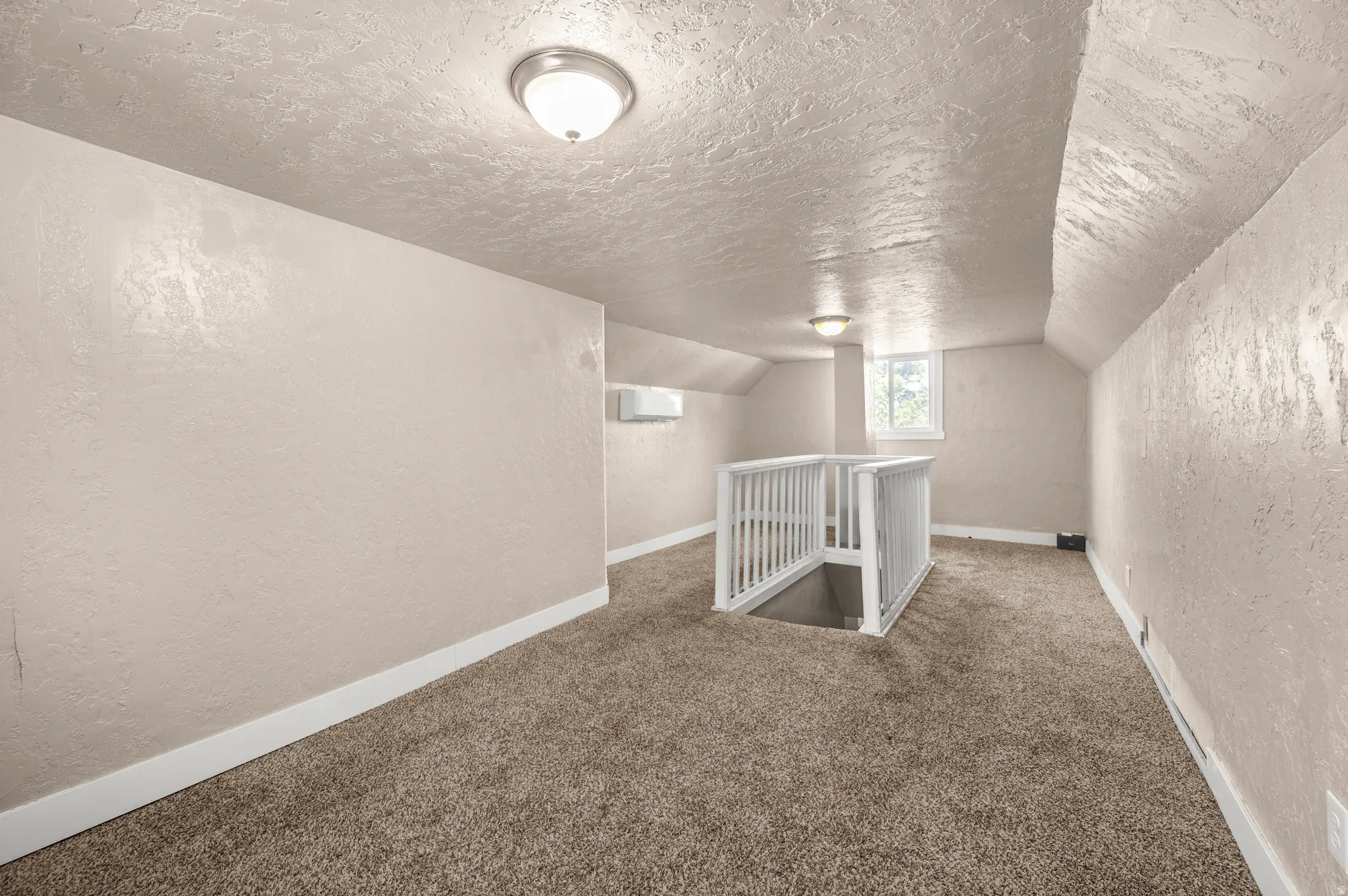 Carpeted upper level featuring a white staircase railing, natural light from a window, and two flush-mount ceiling lights