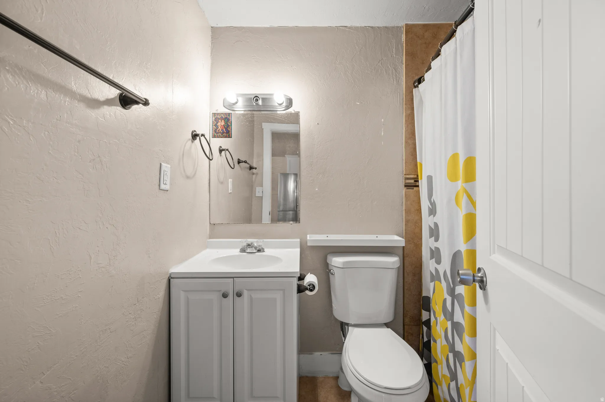 Bathroom featuring a white vanity with integrated sink, a commode, and a shower area with tiled surround