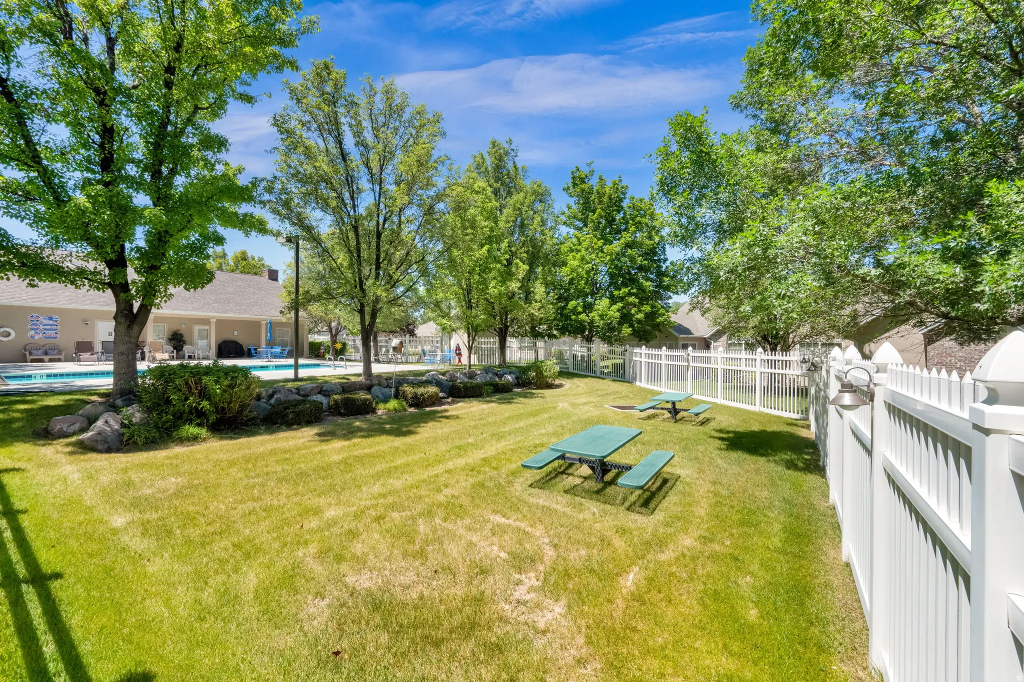 Expansive green space featuring mature trees, a manicured lawn, and a white picket fence