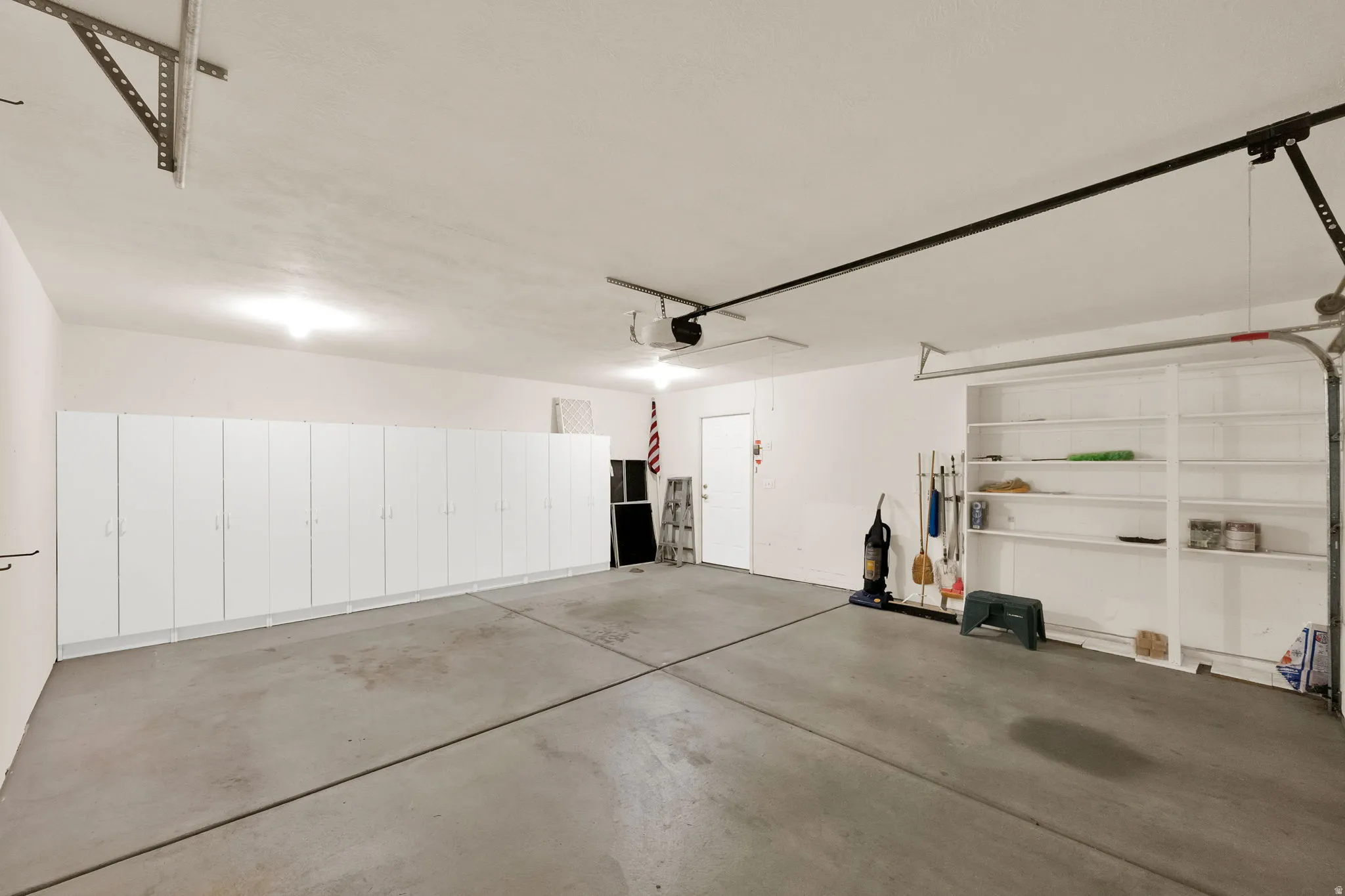 Spacious garage featuring extensive built-in white cabinetry, concrete flooring, overhead lighting, and dedicated shelving