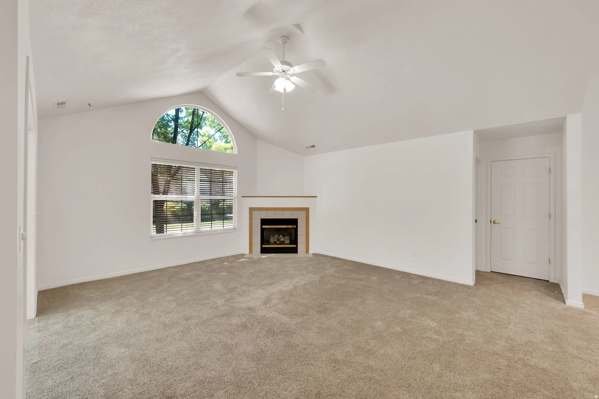Spacious room featuring vaulted ceilings, a prominent arched window, and an integrated fireplace with a light-toned mantel