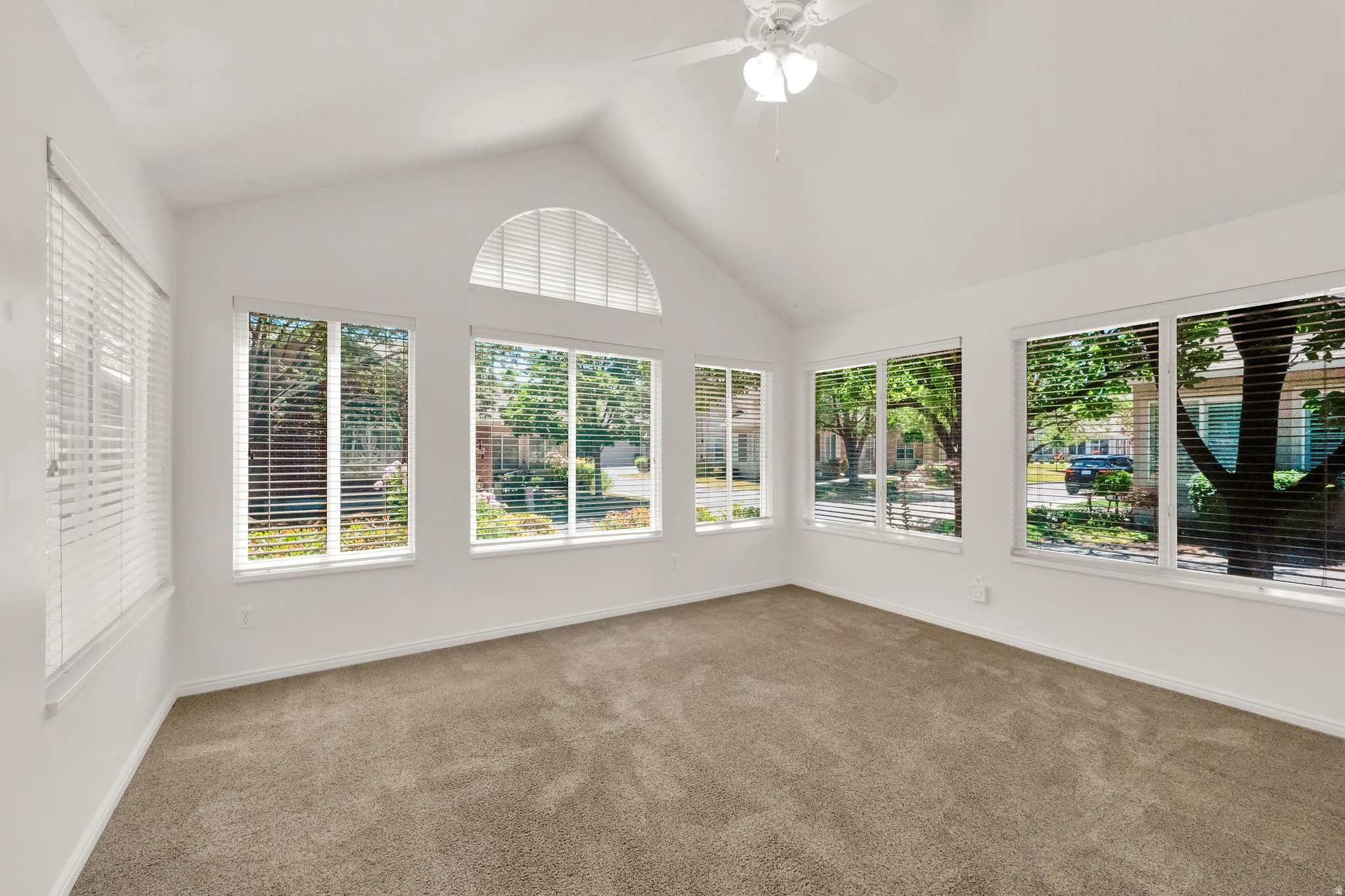 Vaulted ceiling room with multiple windows, an arched transom window, and a ceiling fan