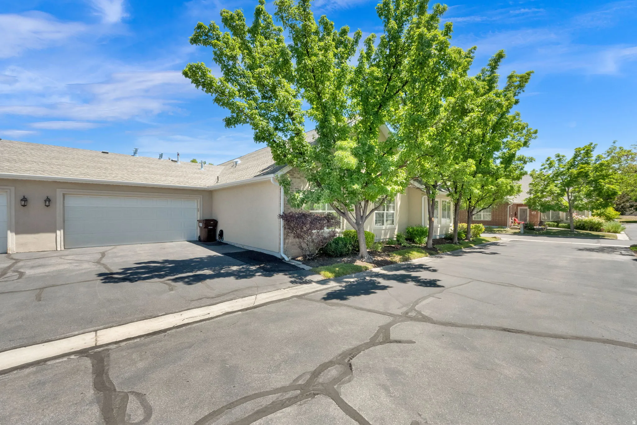 Property exterior featuring a light-colored facade, attached garages, and mature deciduous trees