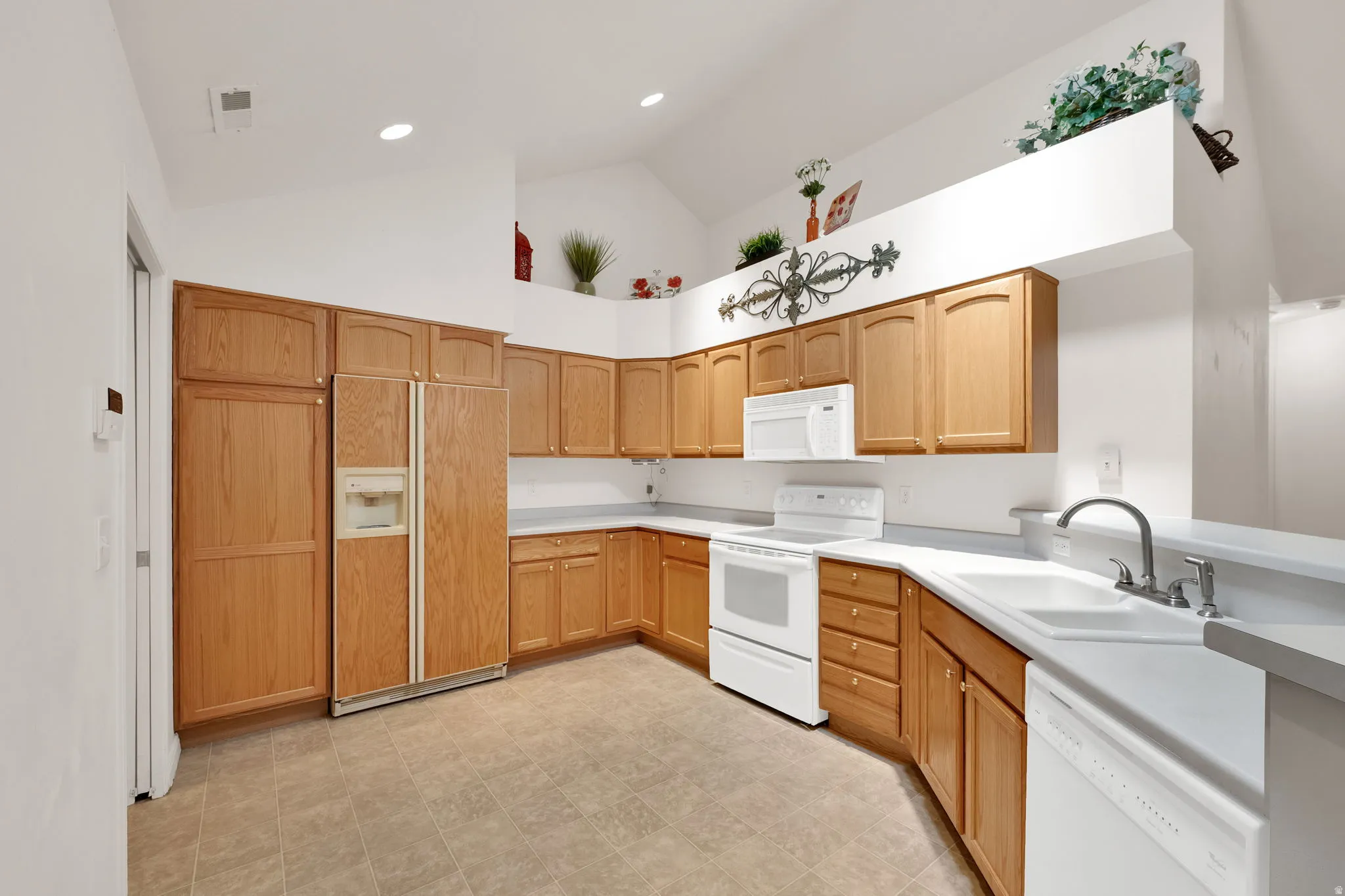 Spacious kitchen featuring light wood cabinetry, white appliances, solid surface countertops, and tile flooring