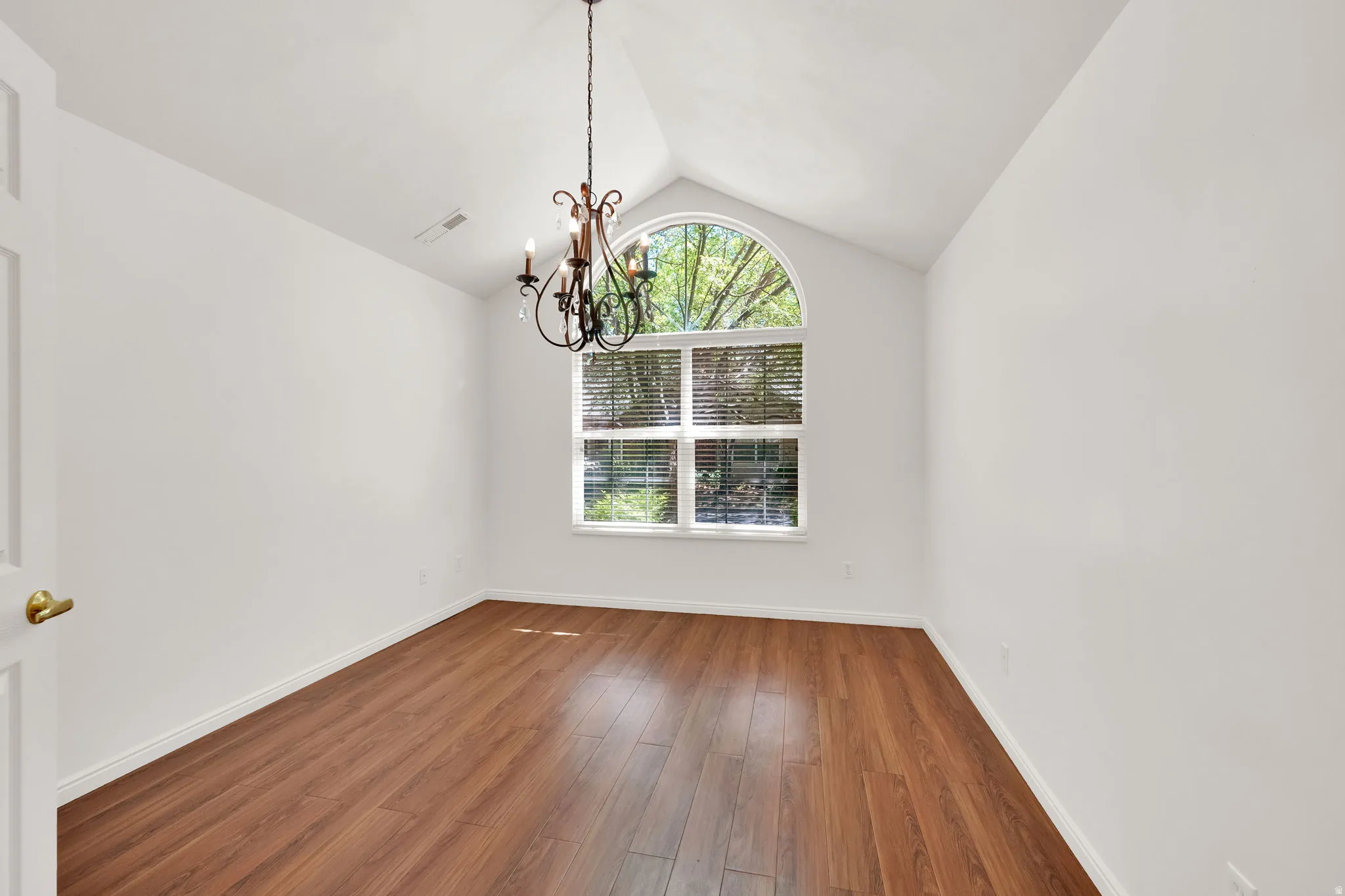 Vaulted ceiling room featuring an arched window, wood-finish flooring, a decorative chandelier, and white baseboards