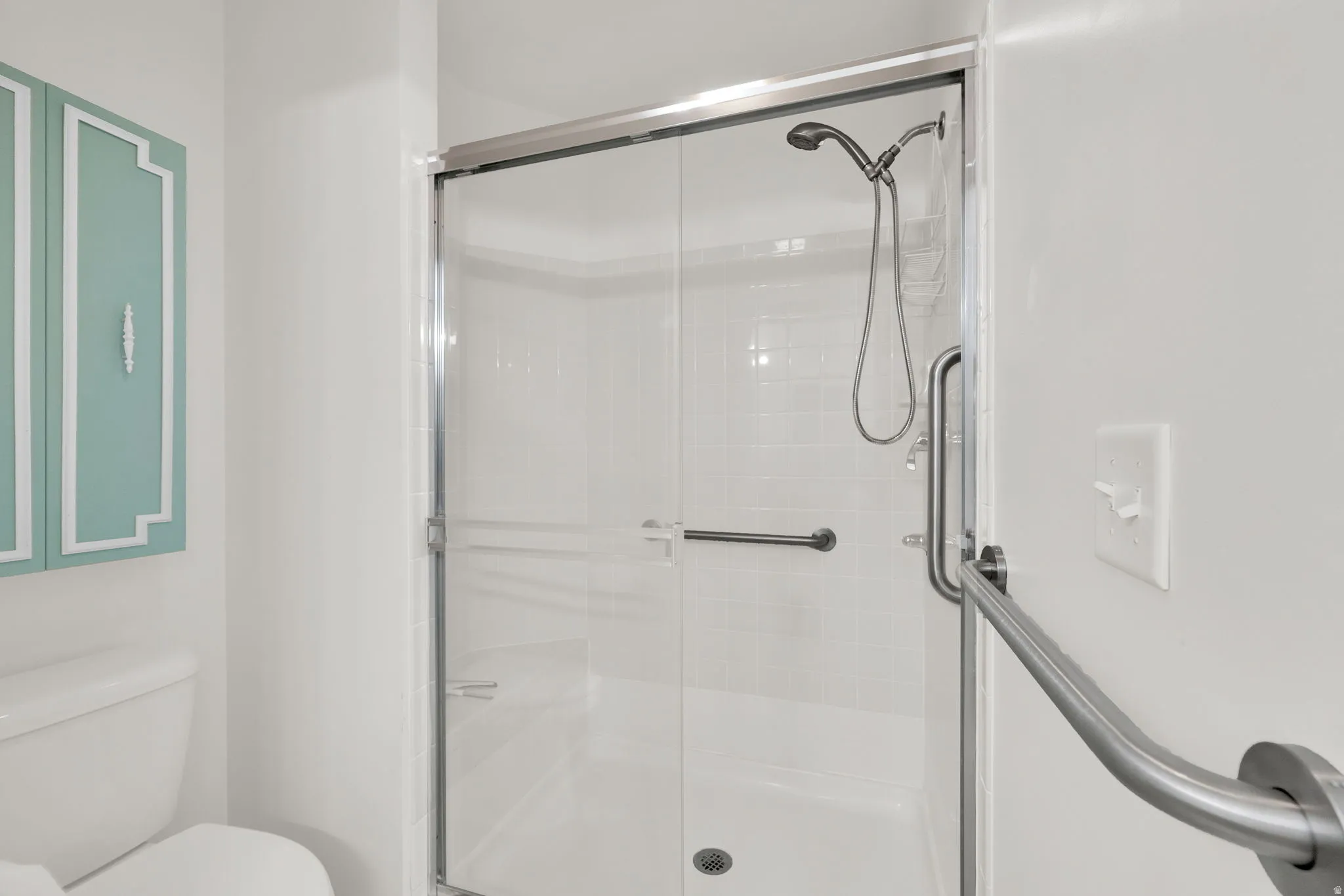Glass-enclosed shower with a white subway tile surround, polished chrome fixtures, and a hand-held shower head