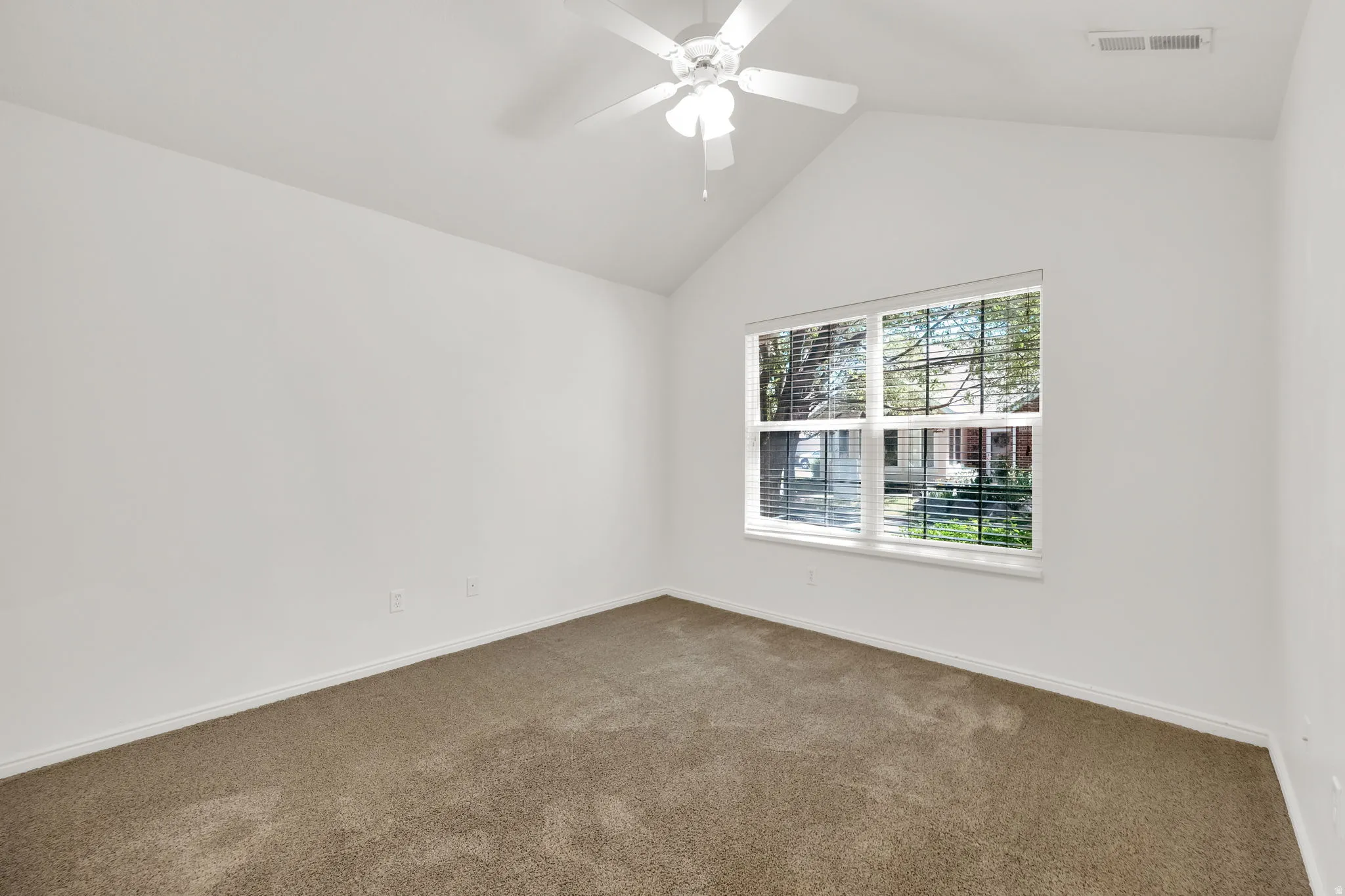 Carpeted room featuring a vaulted ceiling with a ceiling fan, a large window with blinds, and white baseboards