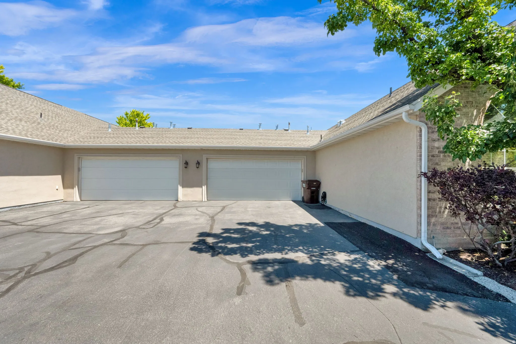 Multi-car garage featuring two white panel garage doors, exterior wall lanterns, and a textured stucco finish