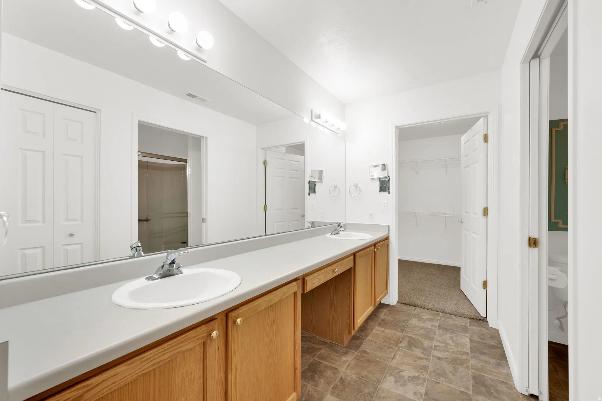 Double vanity featuring twin oval sinks, chrome faucets, and light wood cabinetry with gold-toned hardware