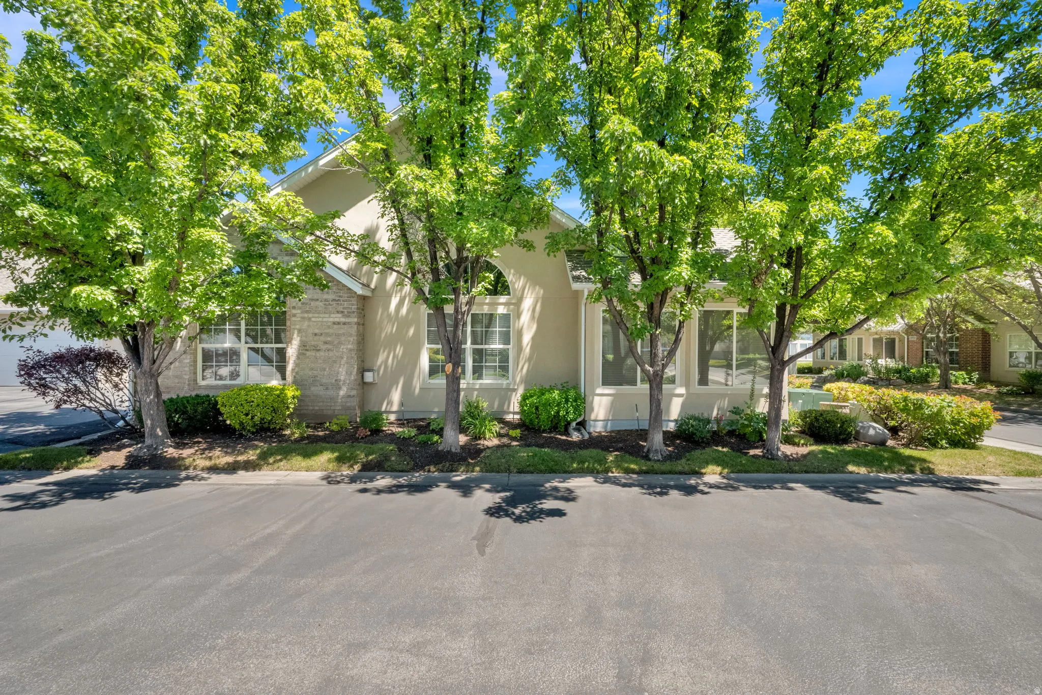 Stucco exterior with stone accents, mature trees, manicured shrubs, and a paved driveway