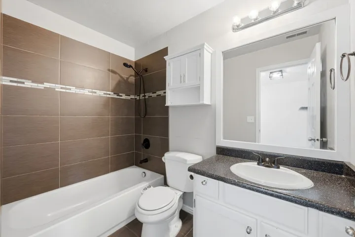 Hall way Bathroom featuring a white tub, dark bronze tile surround with decorative accent band, and a shower fixture
