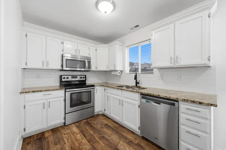 Kitchen featuring white cabinetry, stainless steel appliances, speckled countertops, a white subway tile backsplash, and wood-finish flooring