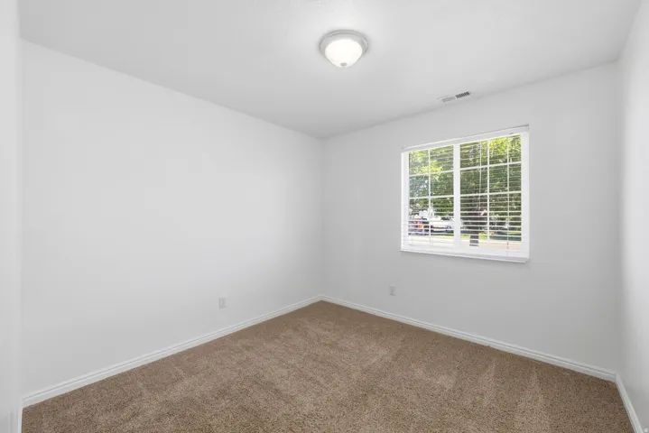 Bedroom 1featuring neutral-toned carpet, white walls, and a large window with blinds