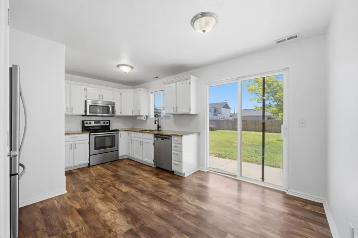 Kitchen featuring white cabinetry, stainless steel appliances, wood-finish flooring, and a sliding glass door to the backyard