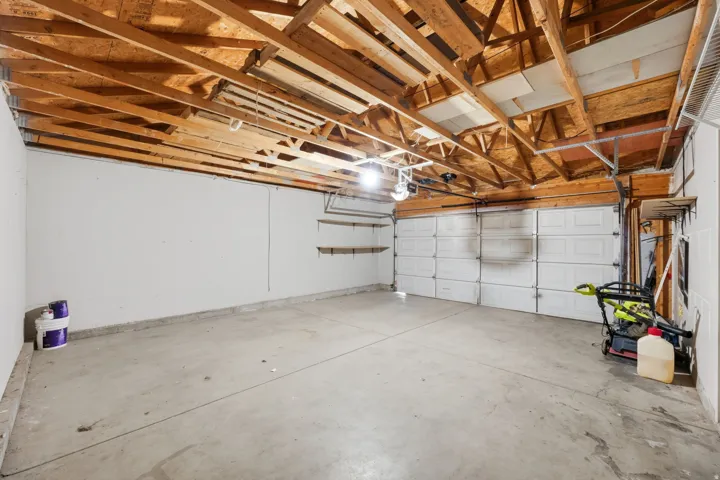 Spacious garage featuring a concrete floor, exposed wood ceiling joists, white walls, and built-in shelving
