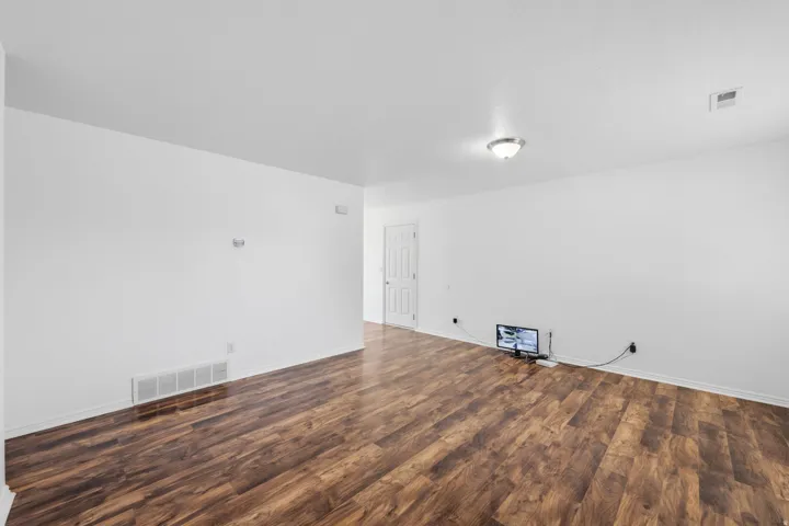Spacious room featuring wood-finish flooring, white walls, and a recessed air vent