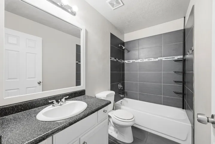 Full master bathroom featuring a white vanity with a dark speckled countertop, an integrated sink, and a chrome faucet