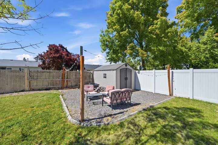 Backyard featuring a gravel patio area with a built-in fire pit, a storage shed, and a privacy fence