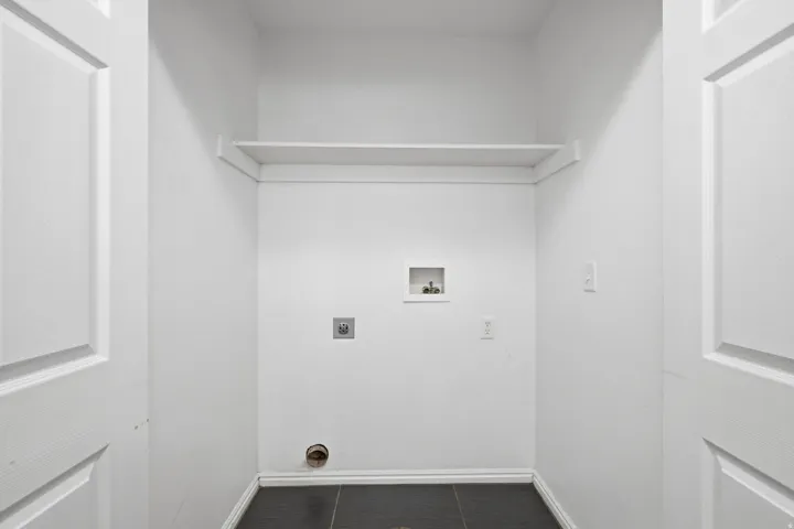 Laundry area featuring dark tile flooring, white walls, and a built-in shelf