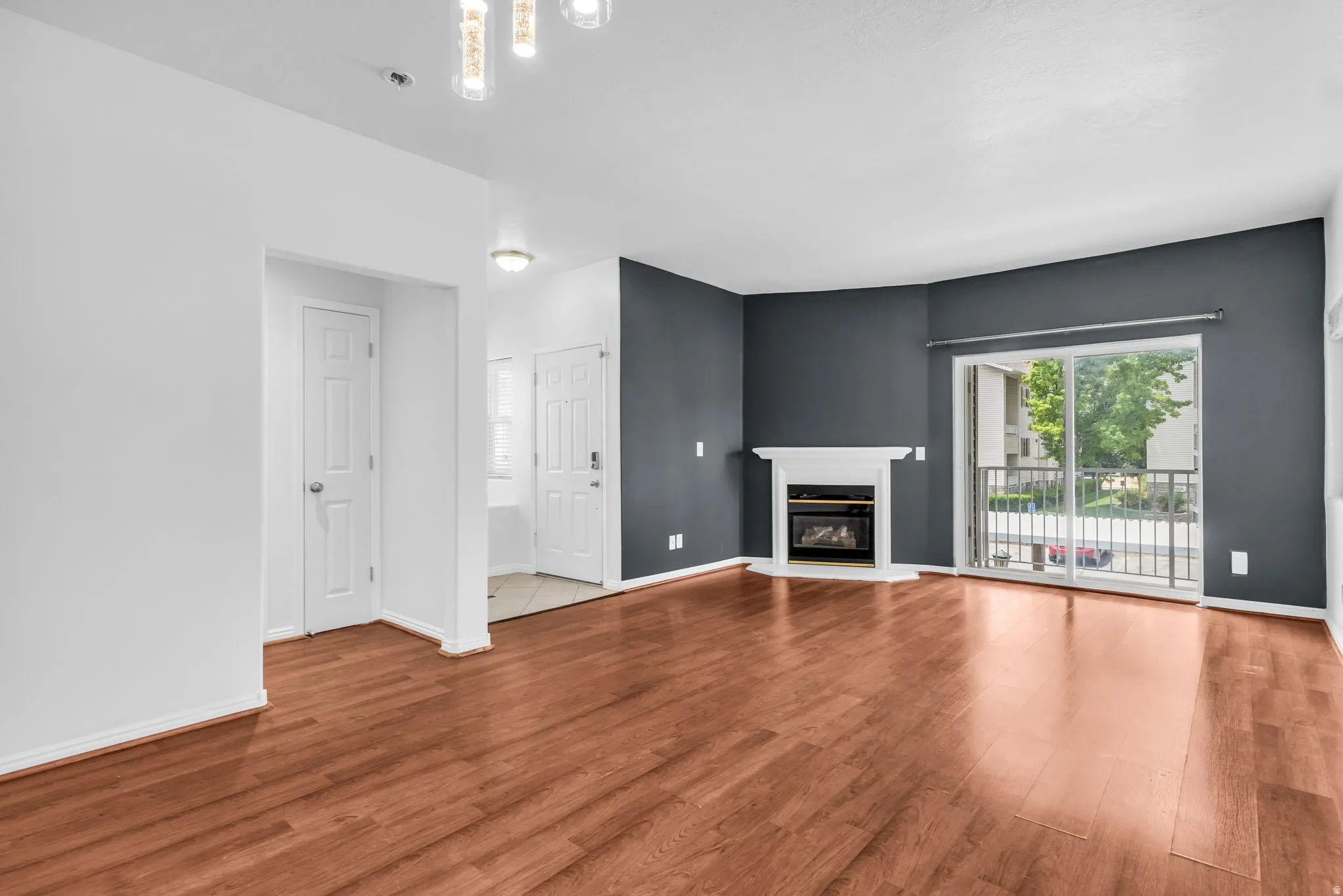 Spacious living area featuring wood-finish flooring, a white mantel fireplace, and a sliding glass door providing exterior access
