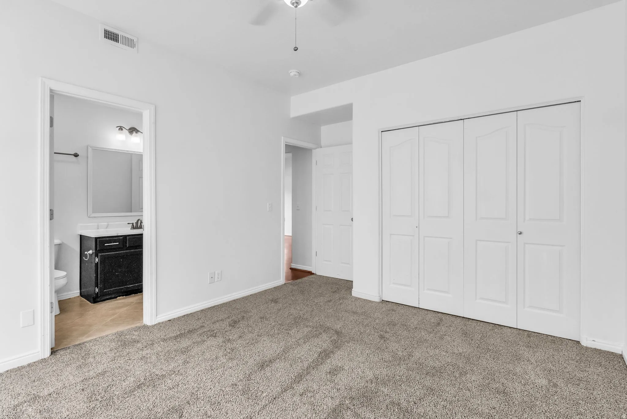 Spacious room featuring neutral carpeting, white walls, and a ceiling fan with integrated lighting