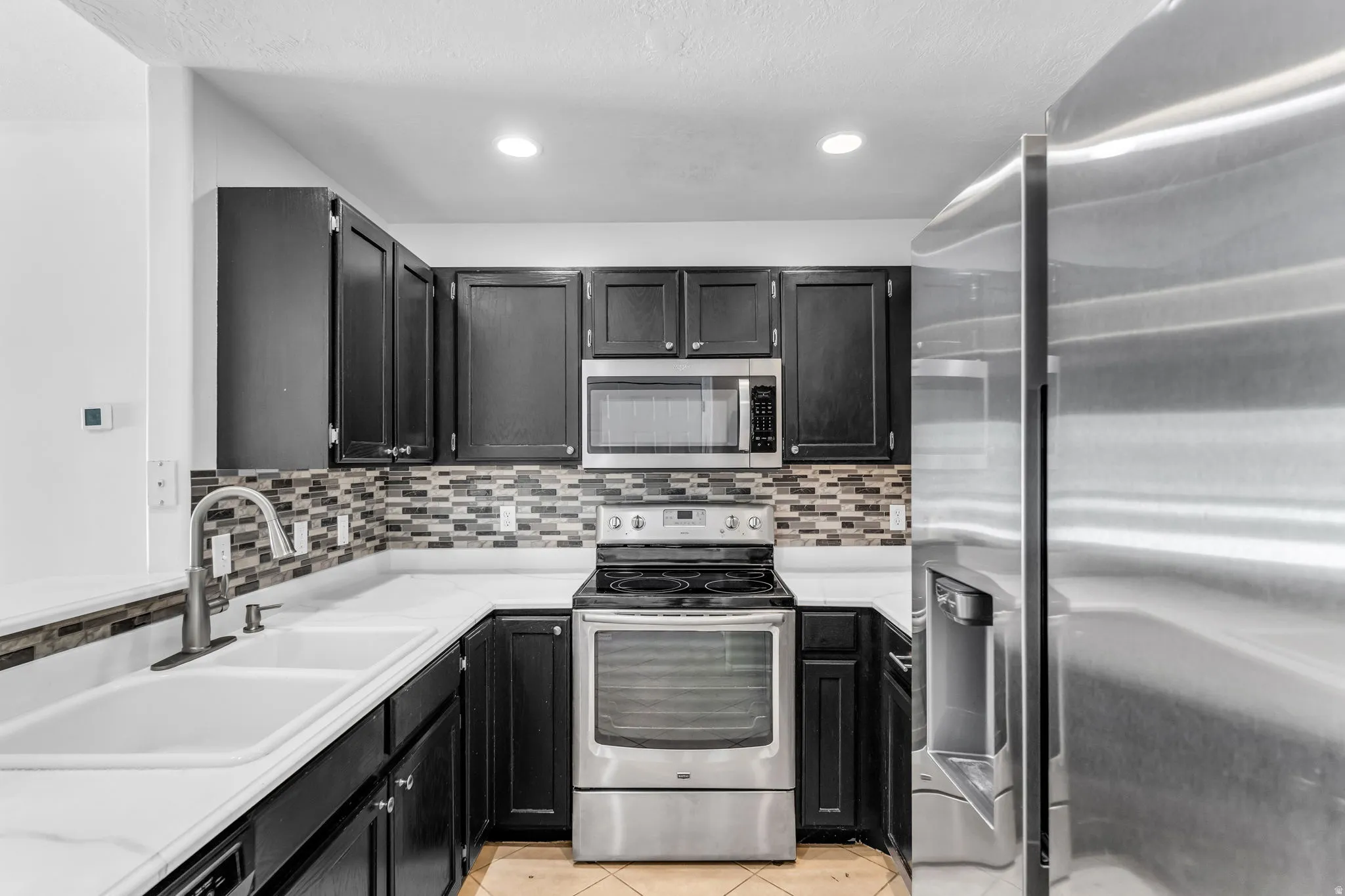 Modern kitchen featuring dark cabinetry, stainless steel appliances, white countertops, and a mosaic tile backsplash