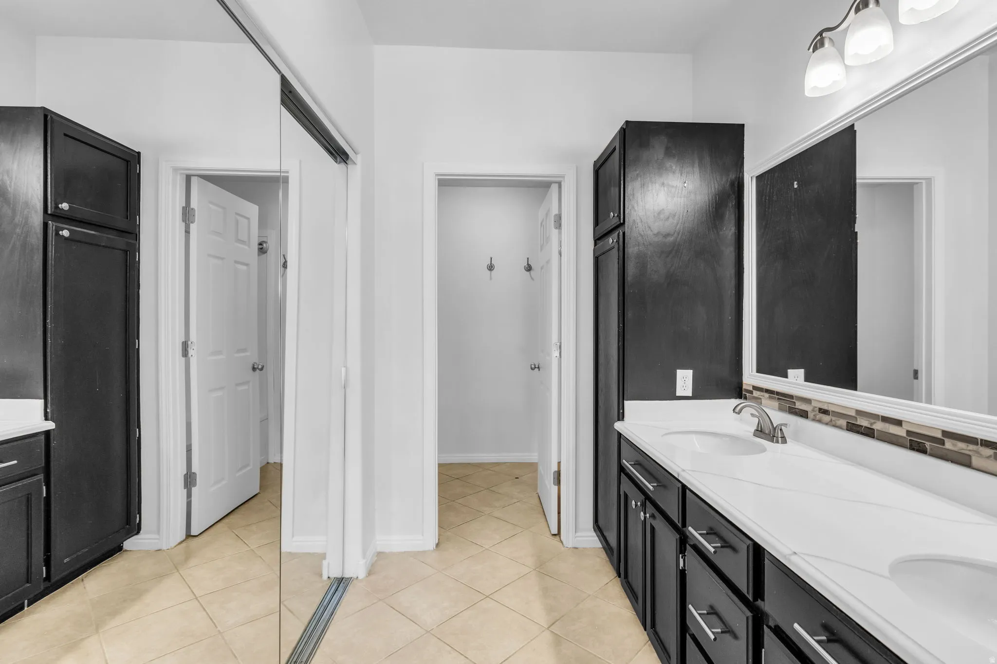 Spacious bathroom featuring dual vanities with white countertops, dark wood-finish cabinetry, and a full-width mirror