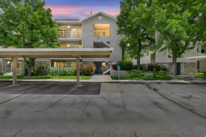 Multi-story residential building with siding and stone accents, featuring covered parking, private balconies, and mature landscaping