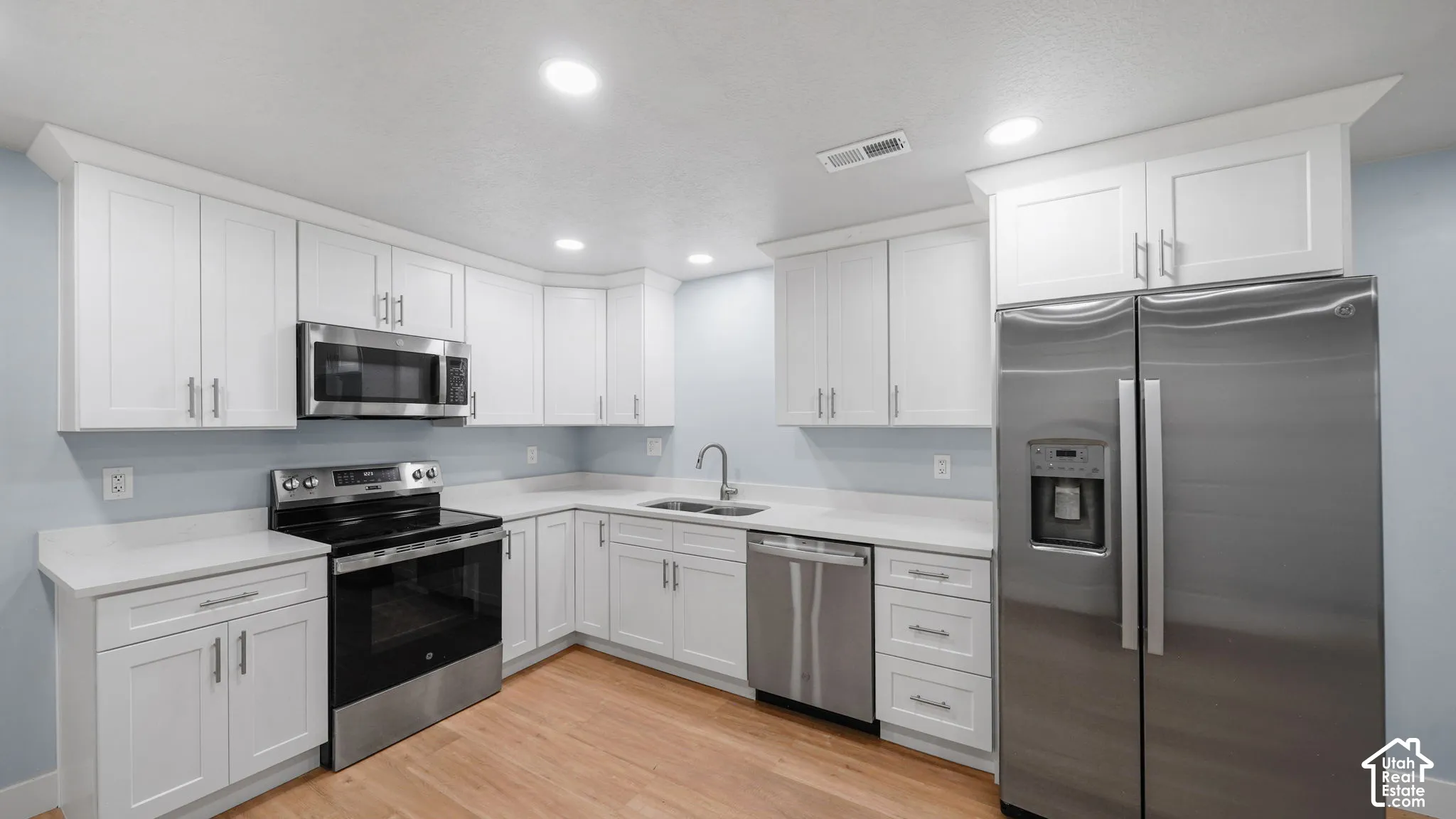 White shaker cabinetry with brushed nickel hardware, stainless steel appliances, light-toned quartz countertops, Luxury Vinyl Plank flooring, and recessed lighting