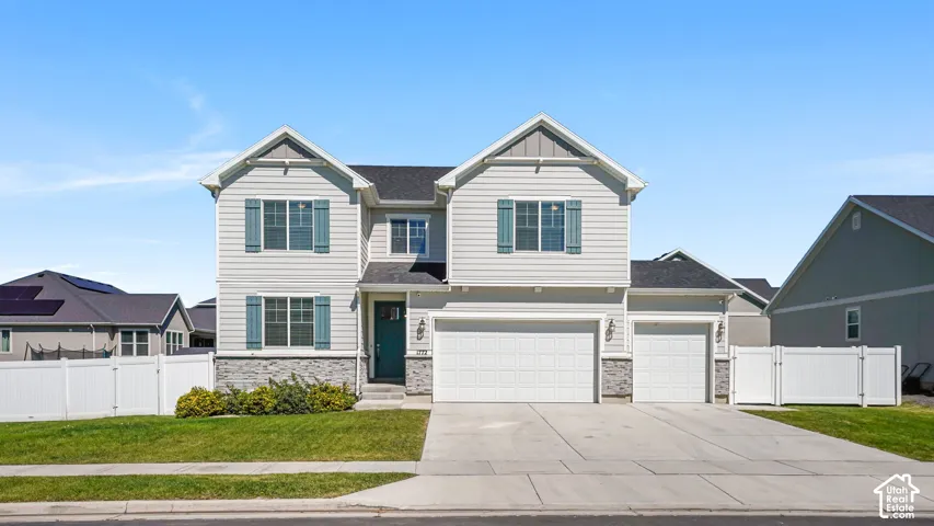 Two-story residence featuring light gray siding, stone veneer accents, and a dual garage