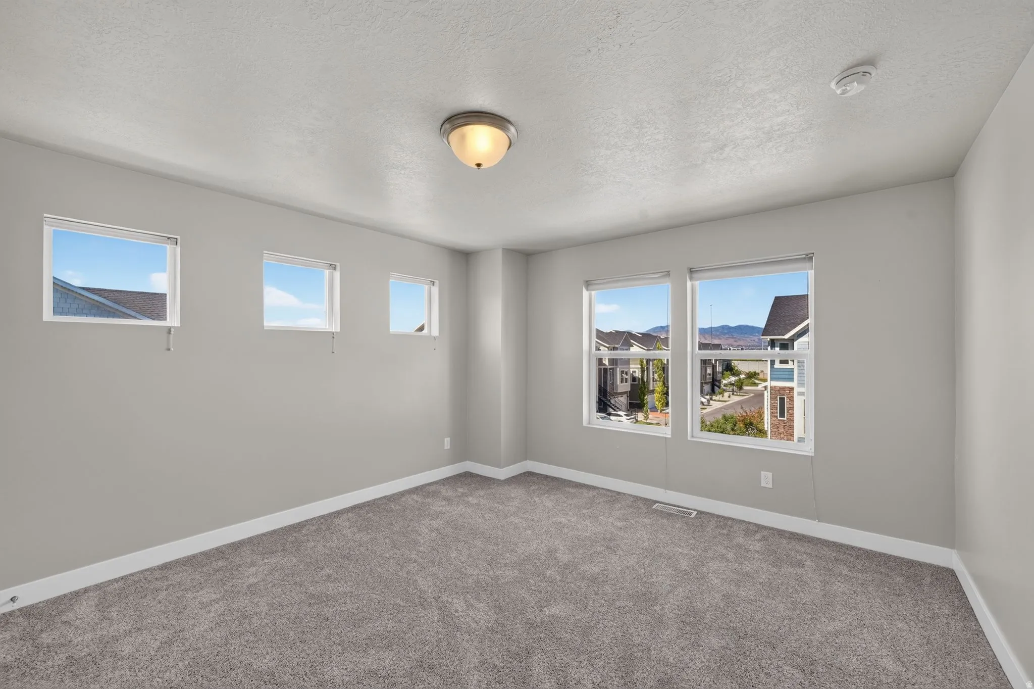 Carpeted room with multiple windows, featuring light gray walls and white trim