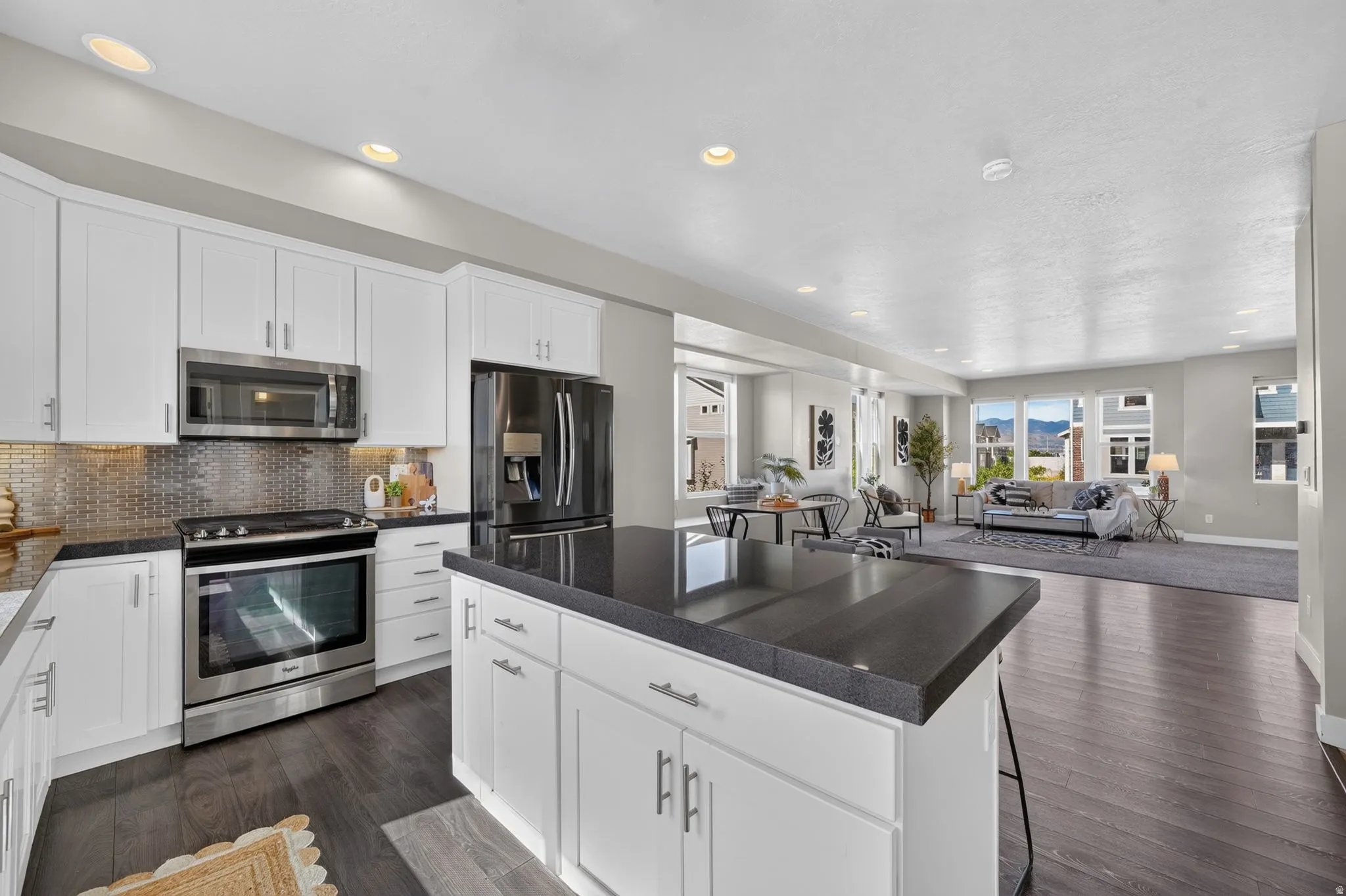 Kitchen featuring white shaker cabinetry, stainless steel appliances, dark countertops, and a textured metal backsplash